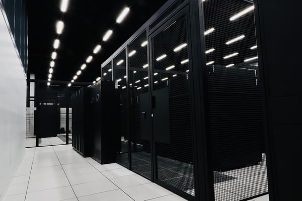 A photograph of a data hall inside of an eStruxture colocation Data Center, showing several rows of black server racks secured within black metal cages. A photograph of a data hall inside of an eStruxture colocation Data Center, showing several rows of black server racks secured within black metal cages.
