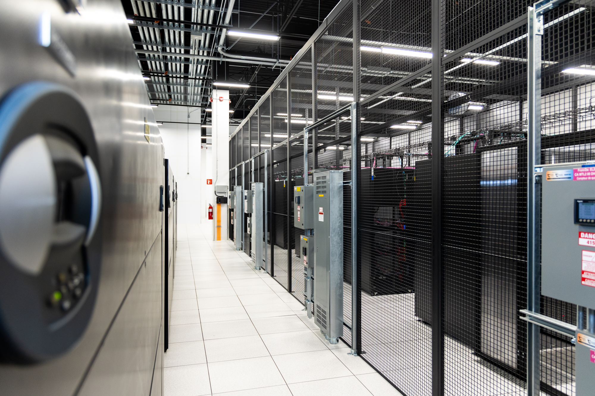 A photograph of a data hall inside of an eStruxture colocation Data Center, showing several rows of black server racks secured within black metal cages.